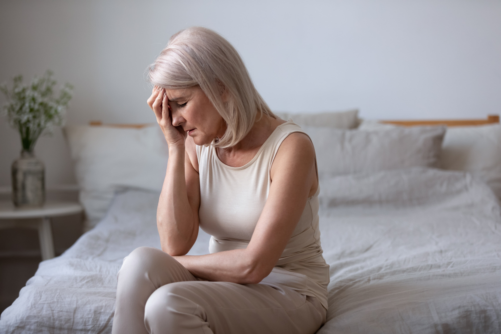 middle aged woman sitting on bed with hand on face